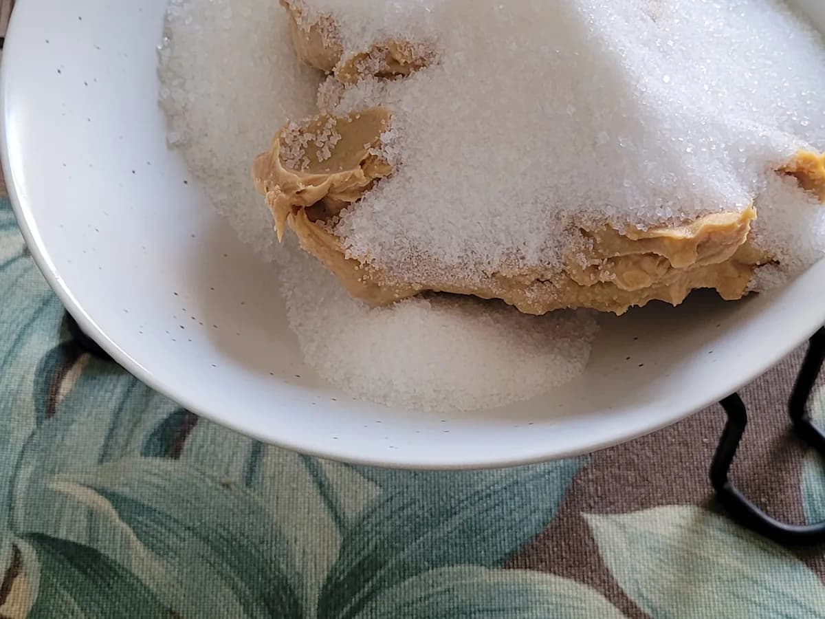Granulated sugar added over creamy peanut butter in a mixing bowl