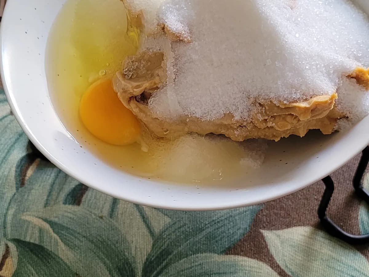 Egg added to peanut butter and sugar in a mixing bowl